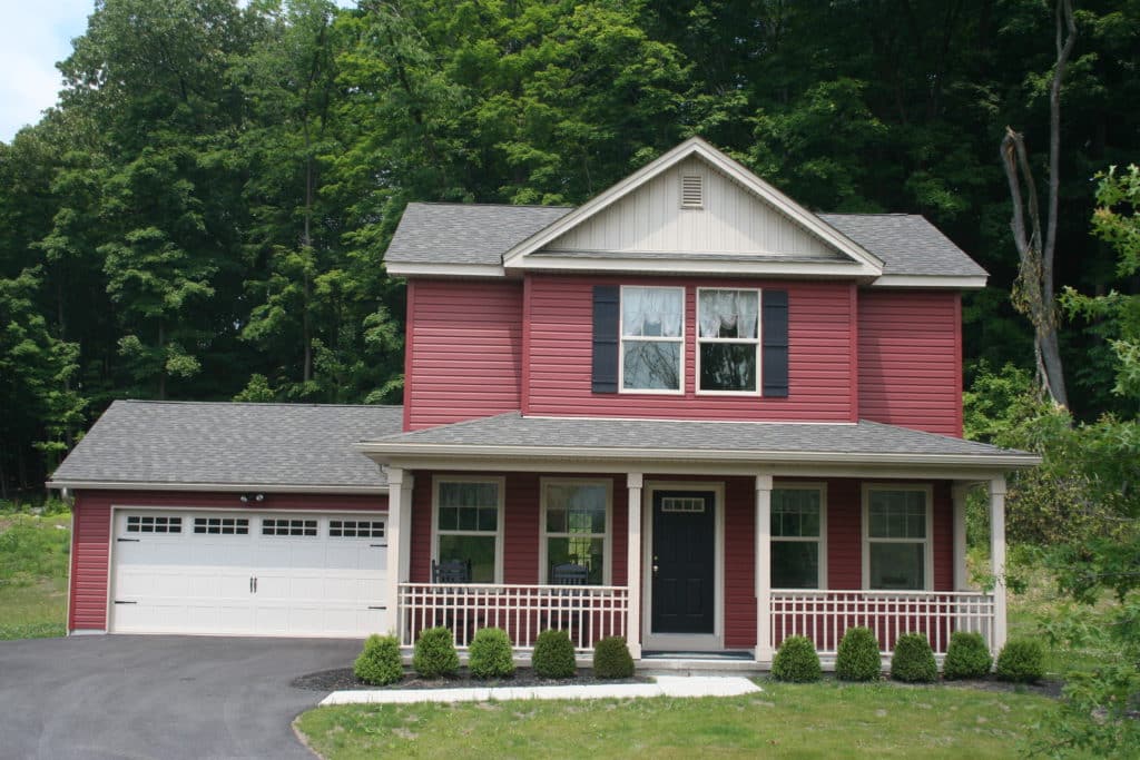 Jasmine home front exterior, 2 story home with red siding, covered front porch and 2-car garage.